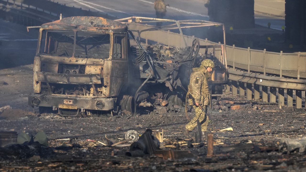 A Ukrainian soldier walks past debris of a burning military truck