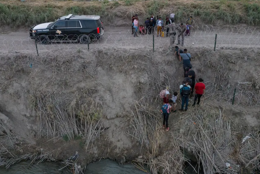 Texas Department of Public Safety troopers pull migrants from under concertina wire after they crossed the Rio Grande from Mexico into Eagle Pass on July 27, 2023. 