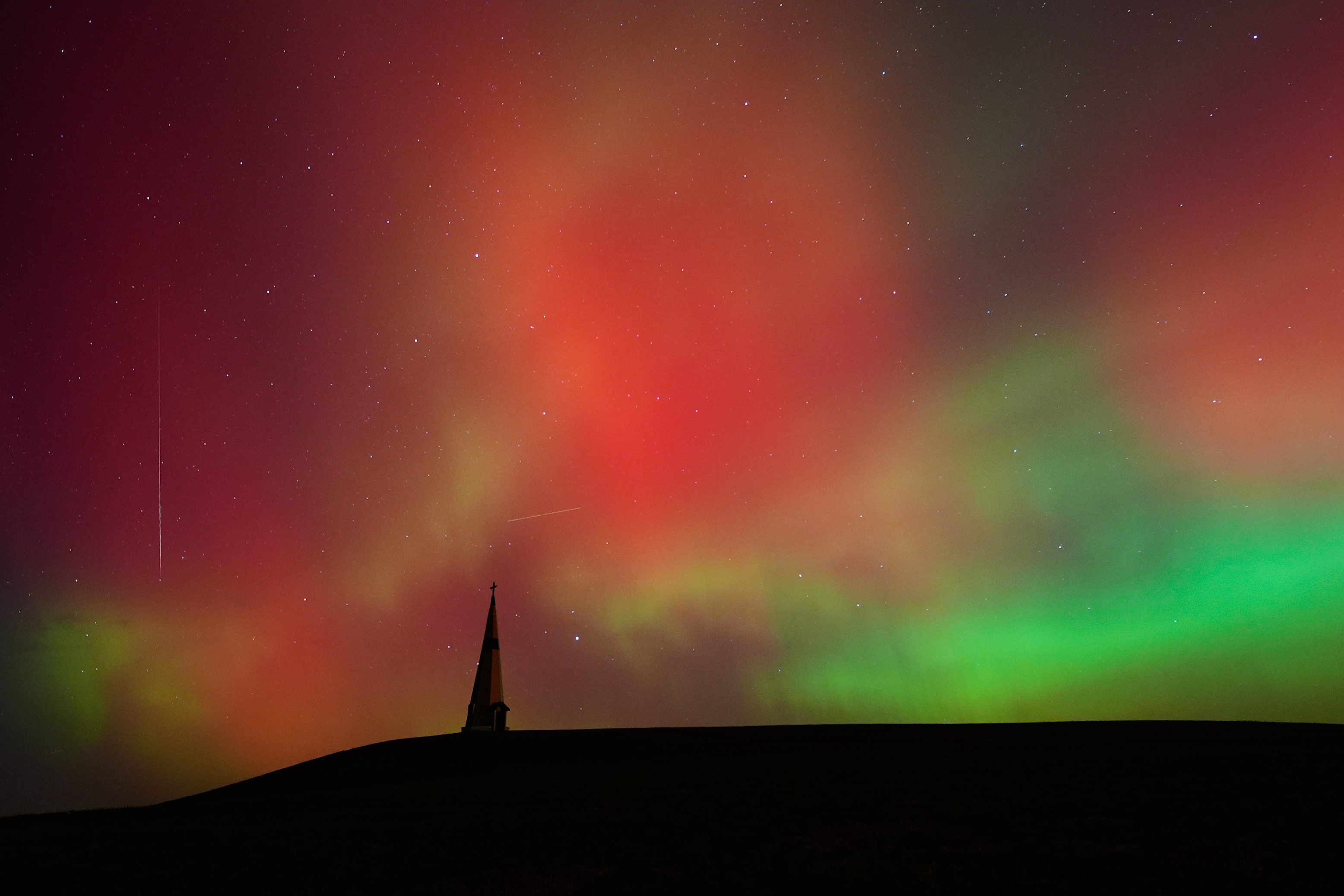 The northern lights along with a shooting star, at left, fill the sky behind the Saint Joseph the Woodworker Shrine Tuesday, Nov. 11, 2025, near Valley Falls, Kan. 