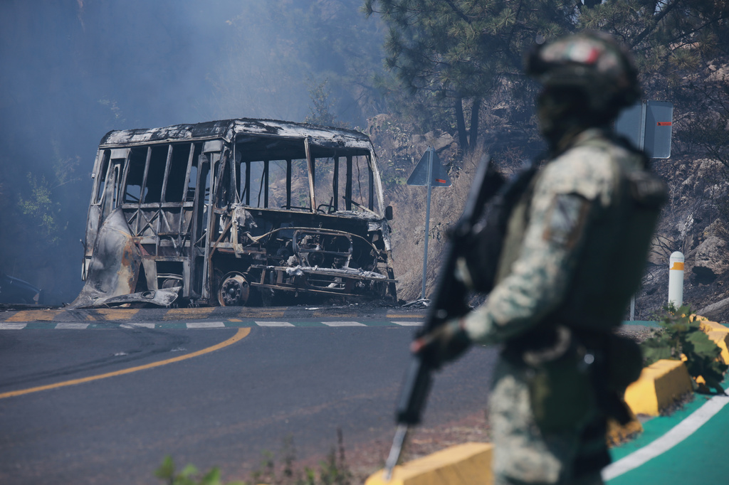 A soldier stands guard by a charred vehicle after it was set on fire, in Cointzio, Michoacán state, Mexico, Sunday, Feb. 22, 2026, following the death of the leader of the Jalisco New Generation Cartel, Nemesio Oseguera, known as "El Mencho." 