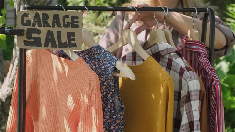 garage-sale-person-looking-for-discounted-apparel-hanging-on-rack-at-garage-sale-SBI-350525444.jpg