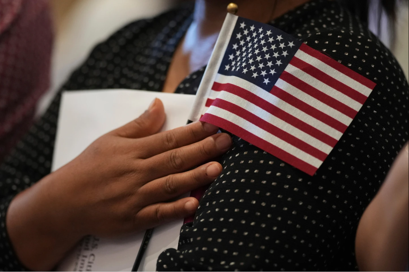 A woman clutches a U.S. flag as she and applicants from other countries prepare to take the oath of citizenship in commemoration of Independence Day during a Naturalization Ceremony in San Antonio, Texas, July 3, 2025.