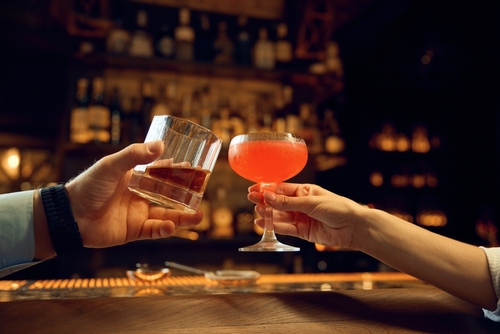 Stock image of male and female hands clinking glasses with alcoholic beverages.