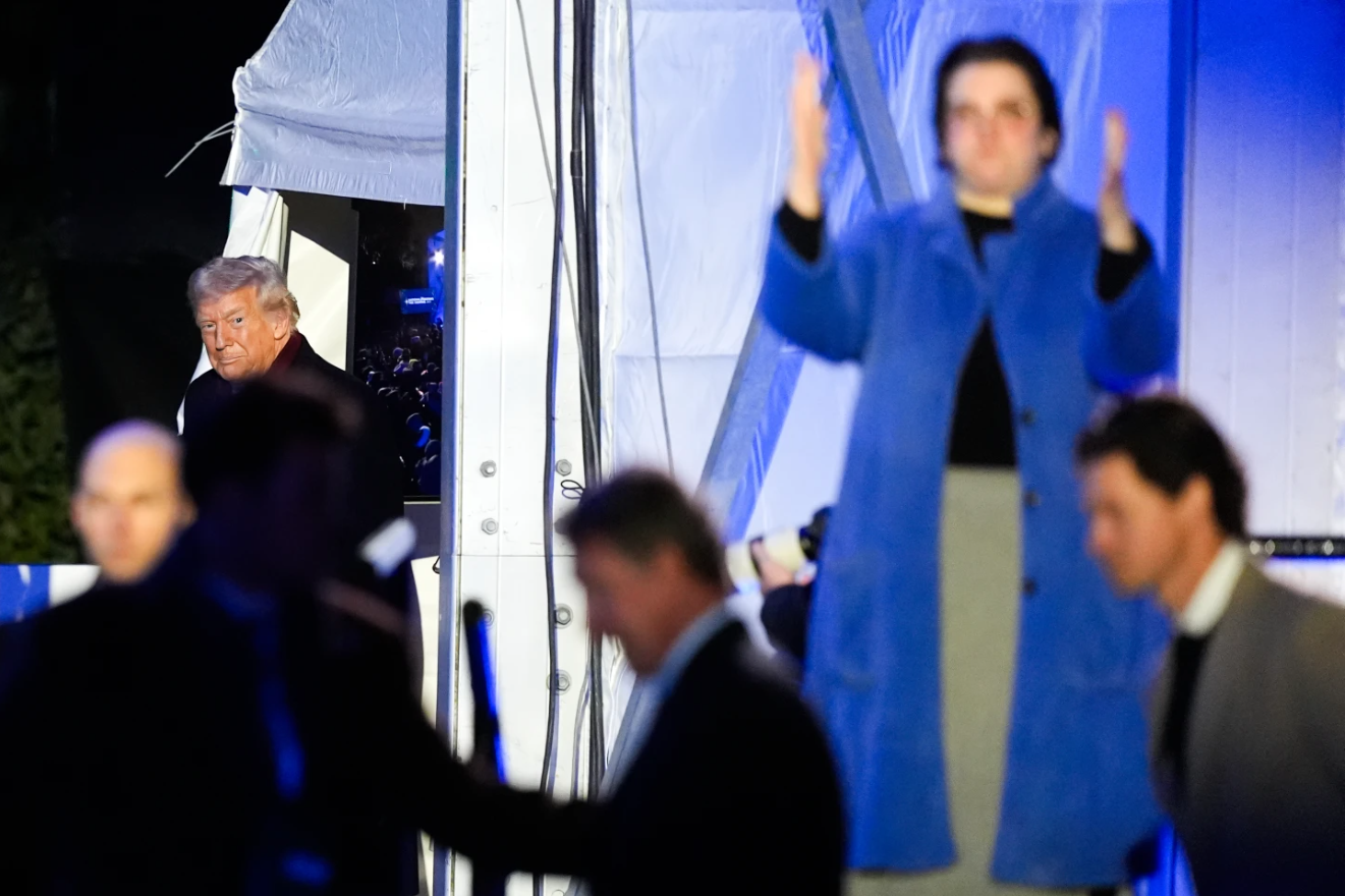 An American Sign Language interpreter, right, signs as President Donald Trump, accompanied by first lady Melania Trump, speaks following the lighting of the National Christmas Treet on the Ellipse, Thursday, Dec. 4, 2025, near the White House in Washington.