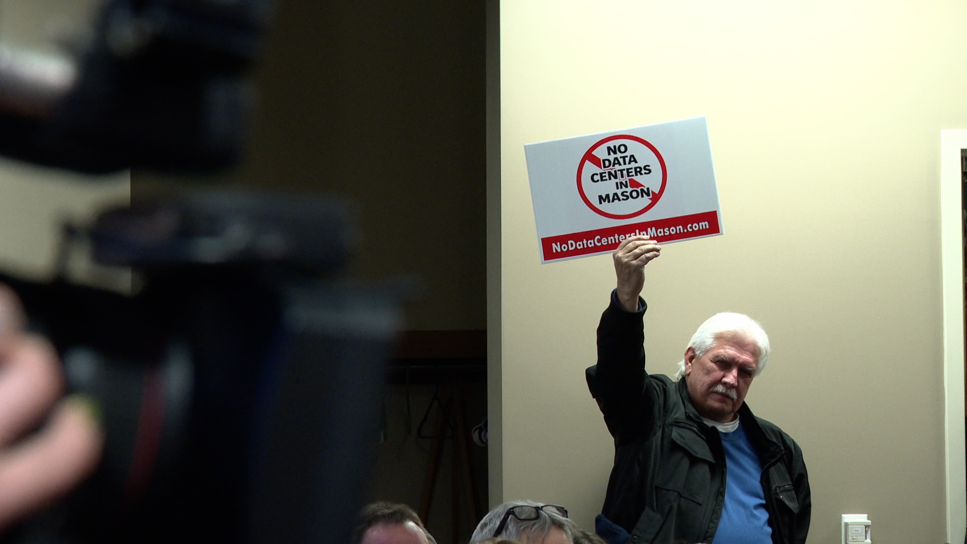 Man holds sign saying 'No Data Centers in Mason' at city council meeting March 16, 2026