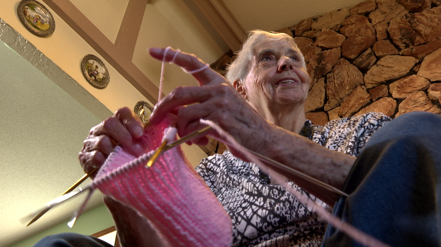 Emmy Christiansen knits a pink cap in her living room.