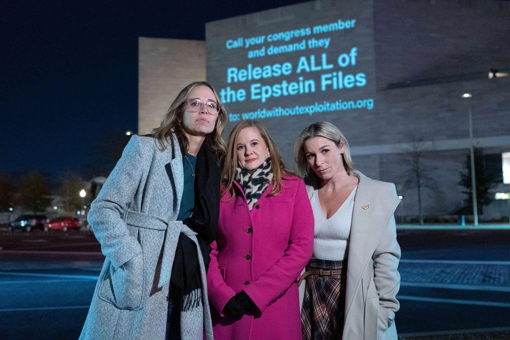 Annie Farmer, from left, Liz Stein and Danielle Bensky pose for a photo as a World Without Exploitation projection is seen on the wall of the National Gallery of Art calling on the Justice Department to release all files it has related to the investigation into Jeffrey Epstein.
