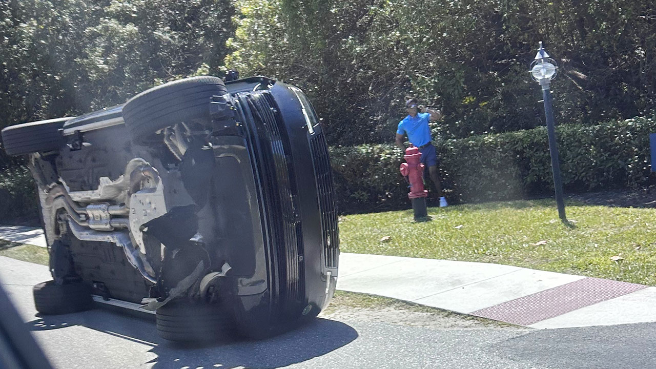 Golfer Tiger Woods stands by his overturned vehicle in Jupiter Island, Fla., on Friday, March 27, 2026. (AP Photo/Jason Oteri)