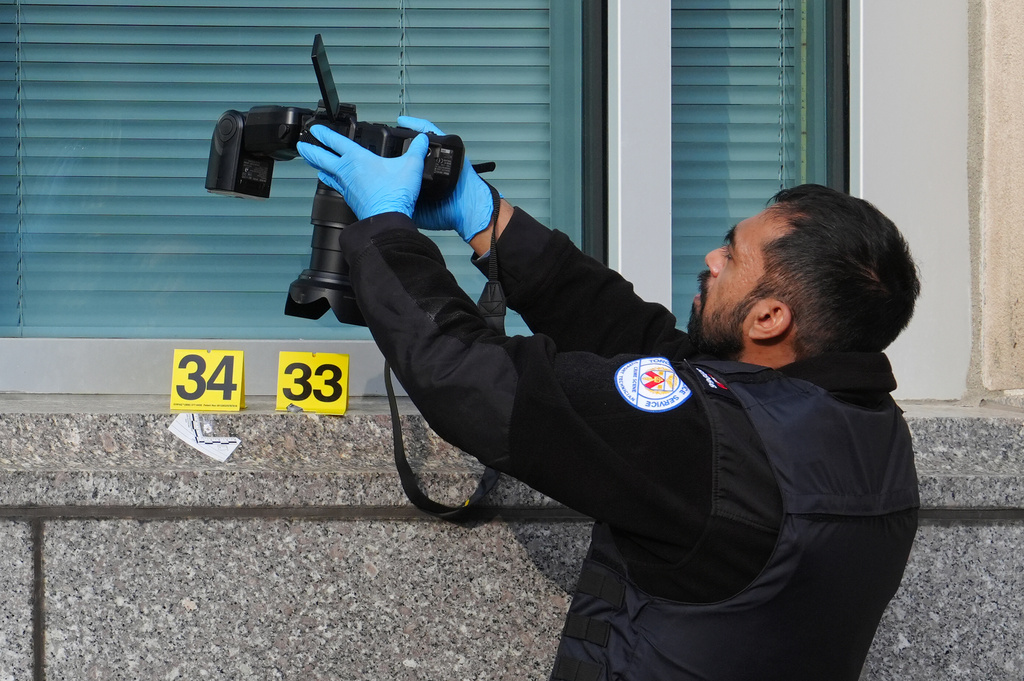 Forensic Toronto police officer photographs bullet impact marks at the front U.S. consulate in Toronto on Tuesday March 10, 2026.
