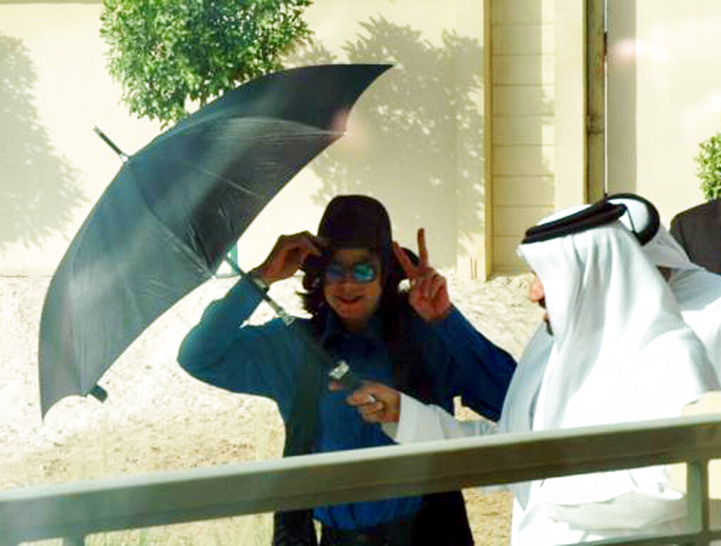 U.S. popstar Michael Jackson shows a victory sign as Mohammed Bin Sulayem, UAE rally champion, holds an umbrella to protect him from sunlight in Dubai, United Arab Emirates.