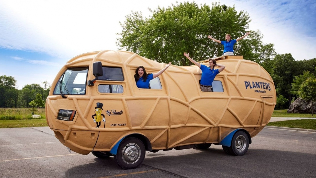 Three people wave from the peanut-shaped Planters NUTmobile.