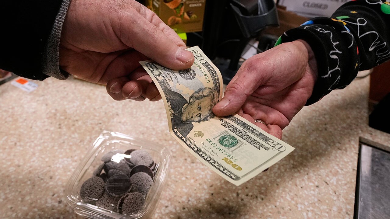 A shopper pays with cash for a container of candy at a store, Thursday, Dec. 11, 2025, in Salem, N.H.