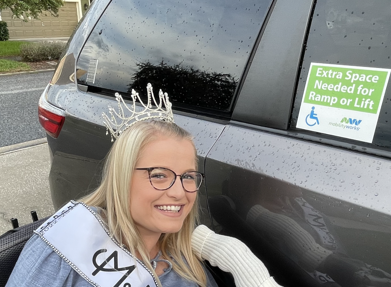Ms. Wheelchair USA next to her car with a sticker on it to let people know she needs extra space to get out