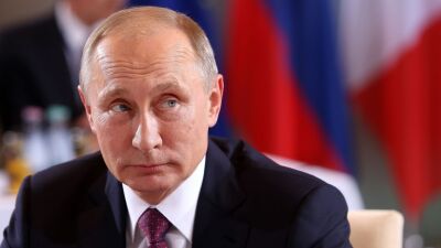 Vladimir Putin sits at a table and looks to his left.
