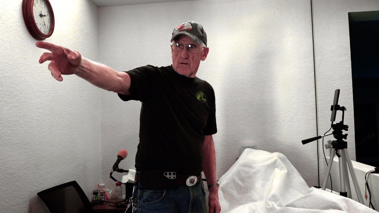 Lee Henderson, Community Chrisitan Church's Elder, inside at his desk pointing towards the bullet damage.