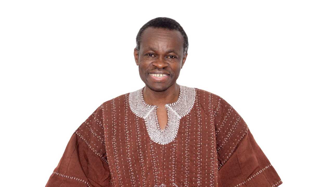 Law professor and activist P.L.O. Lumumba is smiling in this portrait. He is wearing a rust--colored top with white stitching.