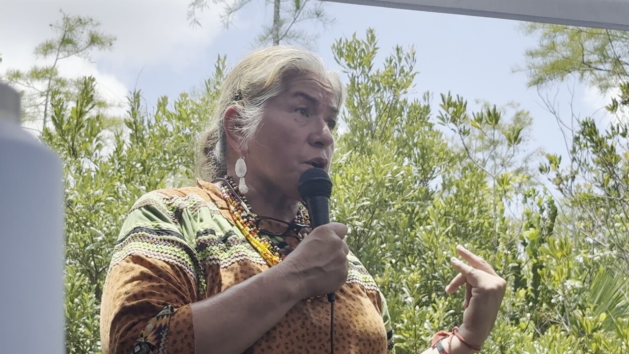 Betty Osceola holds a microphone and addresses the crowd gathered.