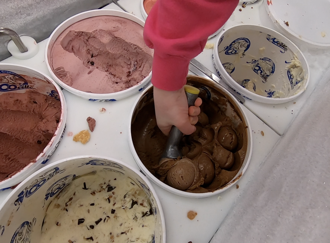 An employee at MOO-ville scooping out chocolate ice cream