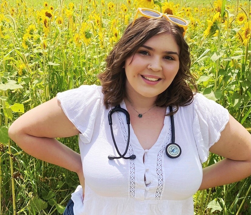 Kaelynn Speed poses with a stethoscope around her neck in a field of sunflowers.
