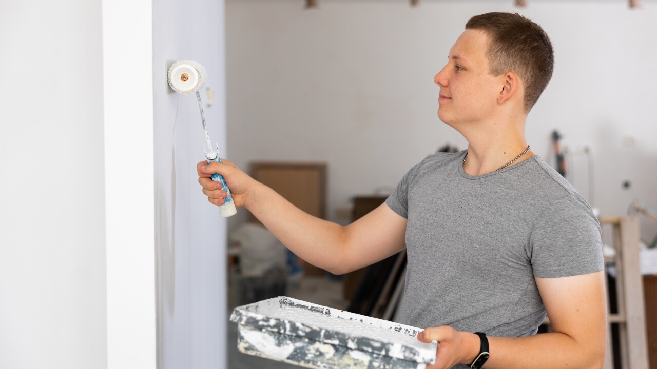 Young,Man,Painting,Wall,With,Paint,Roller,In,Apartment,During