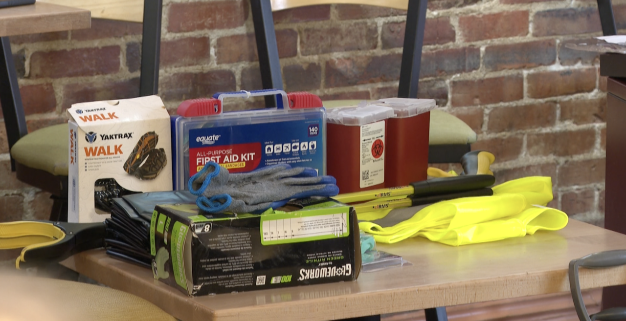 Richards Rubbish Removal Tools- photo of gloves, vest, needle container, all trash pickup gear sitting on a table with a brick background.