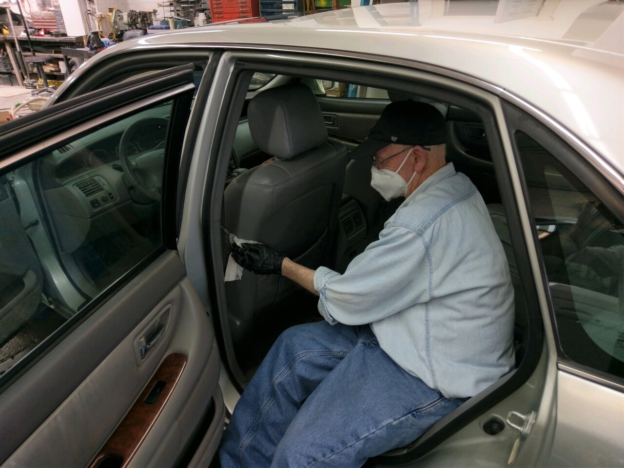 Volunteer Mike Truman helps clean a donated 2000 Toyota Avalon for Samaritan Car Care Clinic. Truman is wearing a mask and gloves while wiping down the driver's seat.