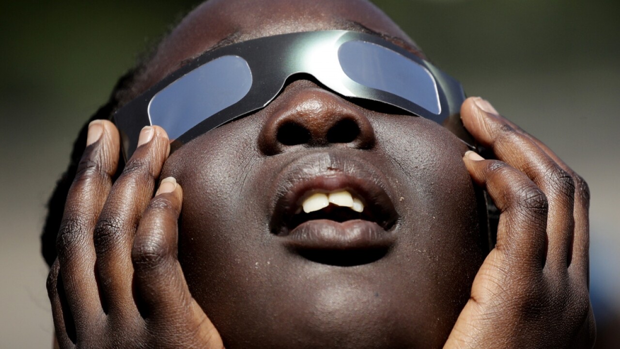 A child looks up through solar eclipse glasses.