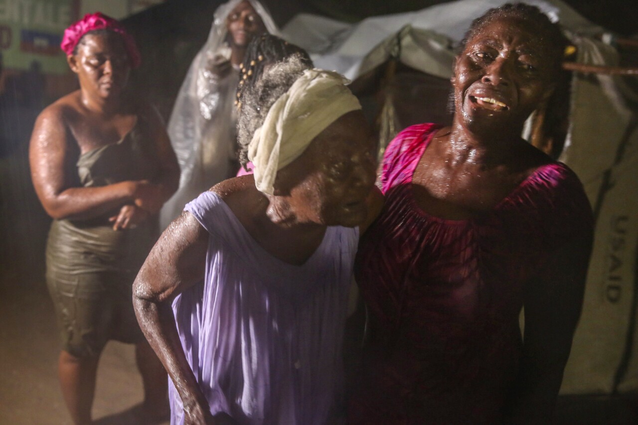 Women affected by Haiti earthquake stand in rain at refugee camp