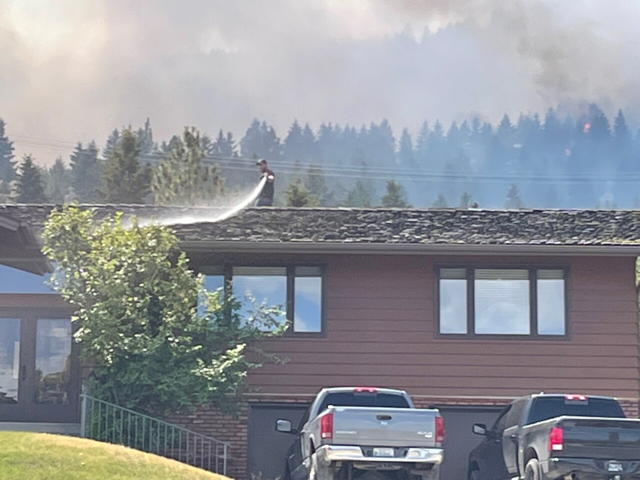 Man spraying roof of a home near wildfire on Mount Helena