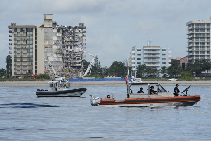 A Coast Guard boat patrols alongside a Miami-Dade County police boat, in front of the partially collapsed Champlain Towers South condo building, ahead of a planned visit to the site by President Joe Biden, on Thursday, July 1, 2021, in Surfside, Fla.jpg