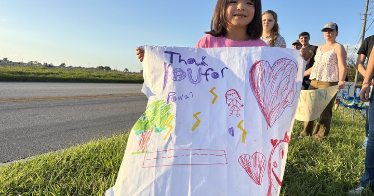 Community lines up with signs to thank parade of lineworkers