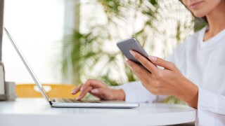 Beautiful young businesswoman using laptop and cell phone in office