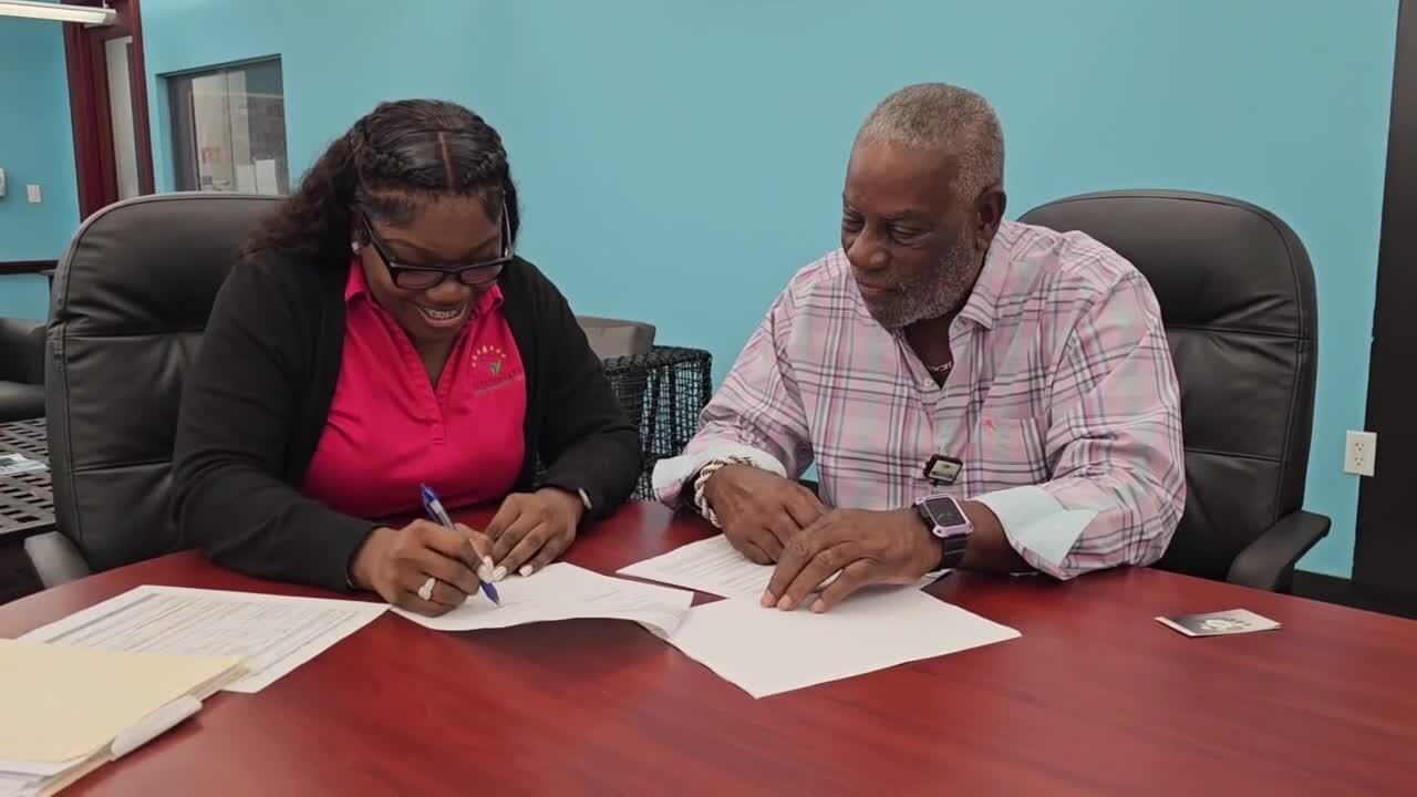 Frank Hayden watches as Michelle Scott signs paperwork to receive West Palm Beach grant for her Passionate Care Services