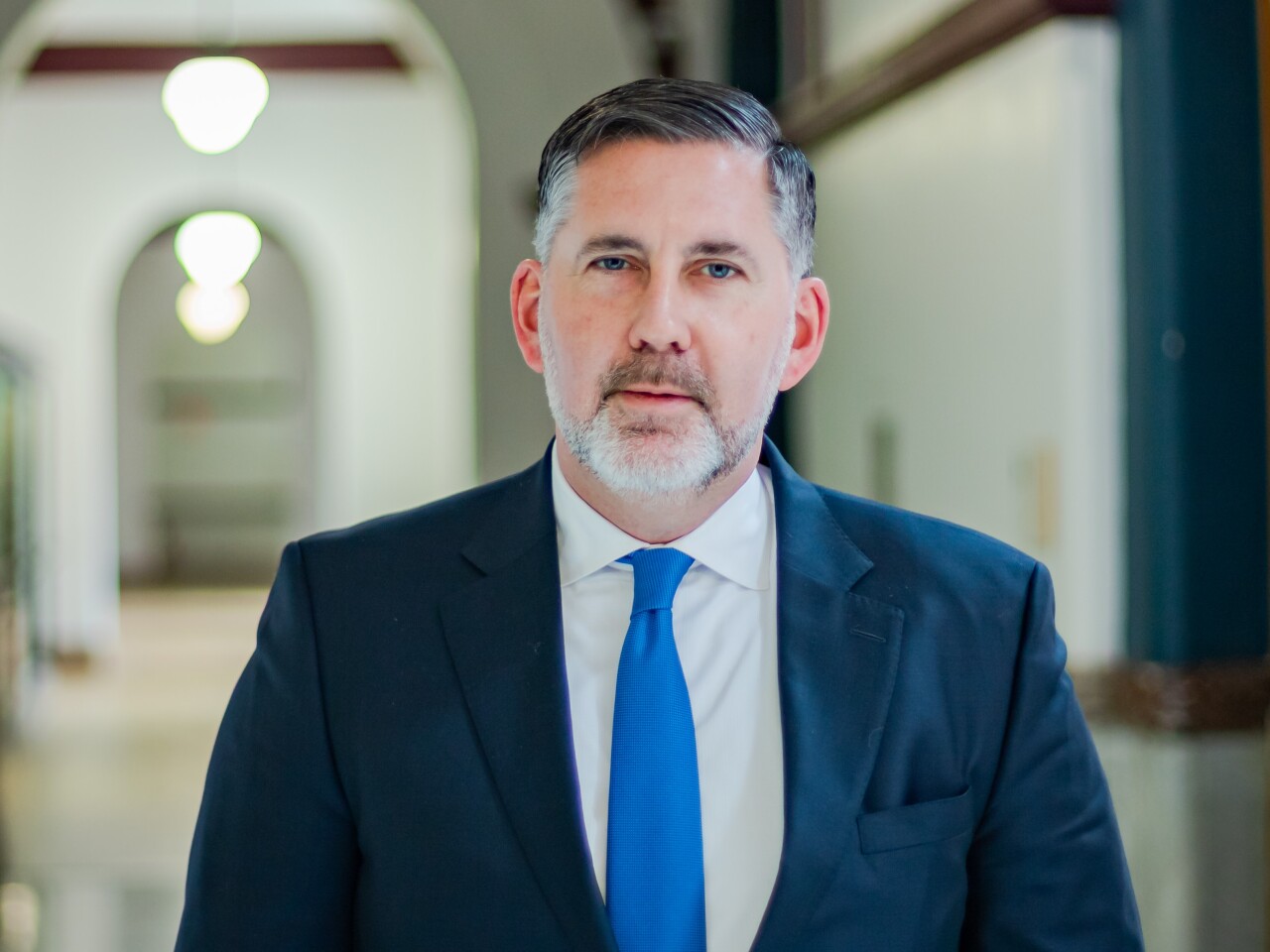 Steve Goodin has short-cropped gray and white hair and a mostly white beard that is trimmed close. He is wearing a royal blue tie, a white shirt and navy suit jacket.