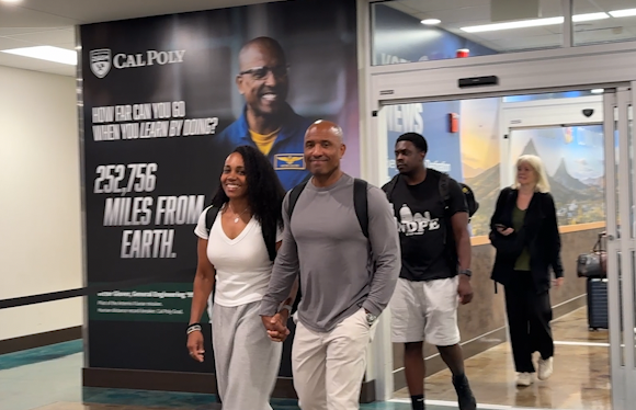 Retired NASA Astronaut and Navy Captain Victor Glover and his wife Dionna arrive in San Luis Obispo, exiting the airport terminal in front of a wall-sized poster of him in his flight spacesuit