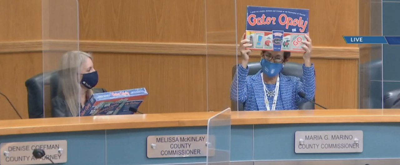 Palm Beach County Commissioner Maria Marino holds up Gatoropoly game while Melissa McKinlay looks on, Nov. 16, 2021
