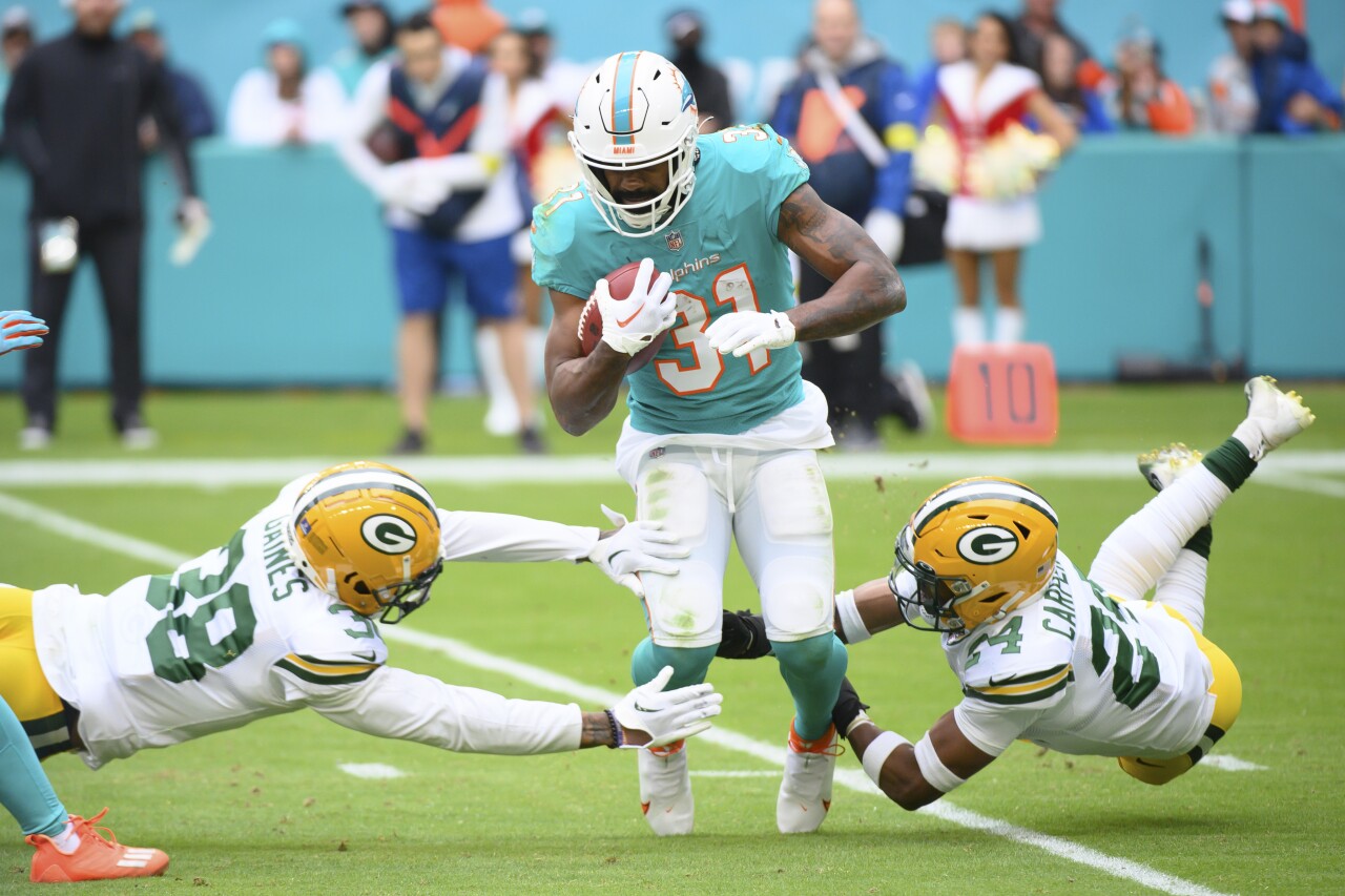 Miami Dolphins running back Raheem Mostert tripped up by Green Bay Packers safeties Innis Gaines and Tariq Carpenter, Dec. 25, 2022