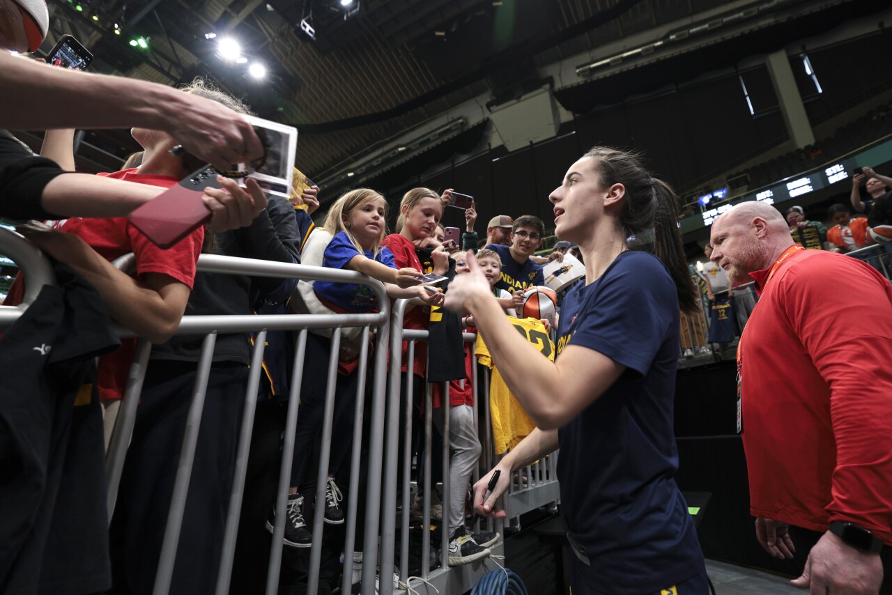 Indiana Fever guard Caitlin Clark signs autographs for fans at a WNBA game.