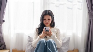 Young,Asian,Woman,Sitting,On,Bed,Using,Smartphone,Mobile,Phone