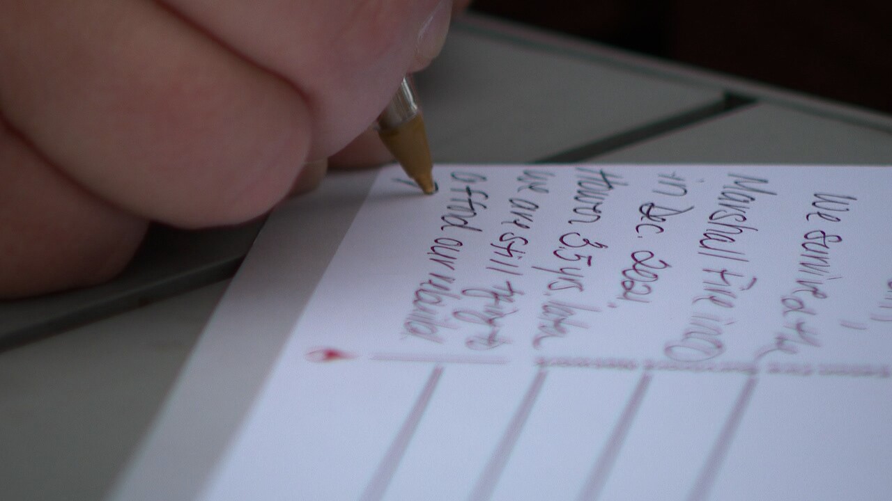 Close-up of a neighbor writing a postcard to a lawmaker about the experience of surviving the Marshall Fire.