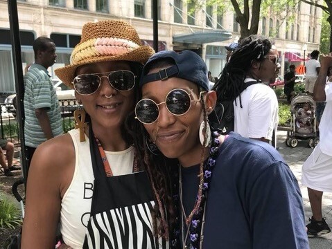 In this undated photo taken outdoors, Jennie Wright, on the left, and her daughter, Siri Imani, are leaning into each other and smiling. Both are wearing sunglasses. Wright is wearing a woven hat, and Imani is wearing a black ball cap backward.
