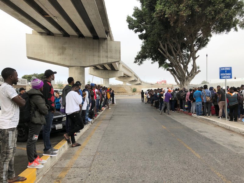 In this July 26, 2019 photo, a group of migrants in Tijuana, Mexico, listen to numbers being called for people to claim asylum in the U.S. The long waits are starting to test the patience of immigrants and border towns. (AP Photo/Elliot Spagat)
