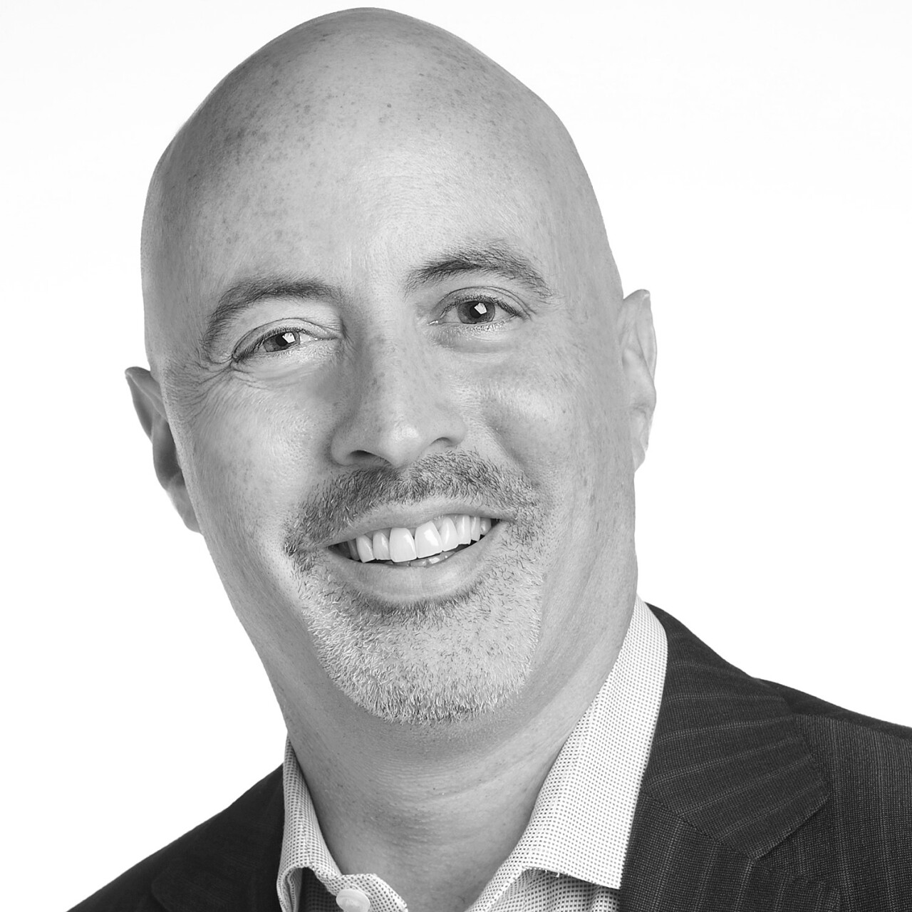 Daniel Epstein is smiling in this portrait. His head is shaved, and he has a short-cropped beard and mustache.