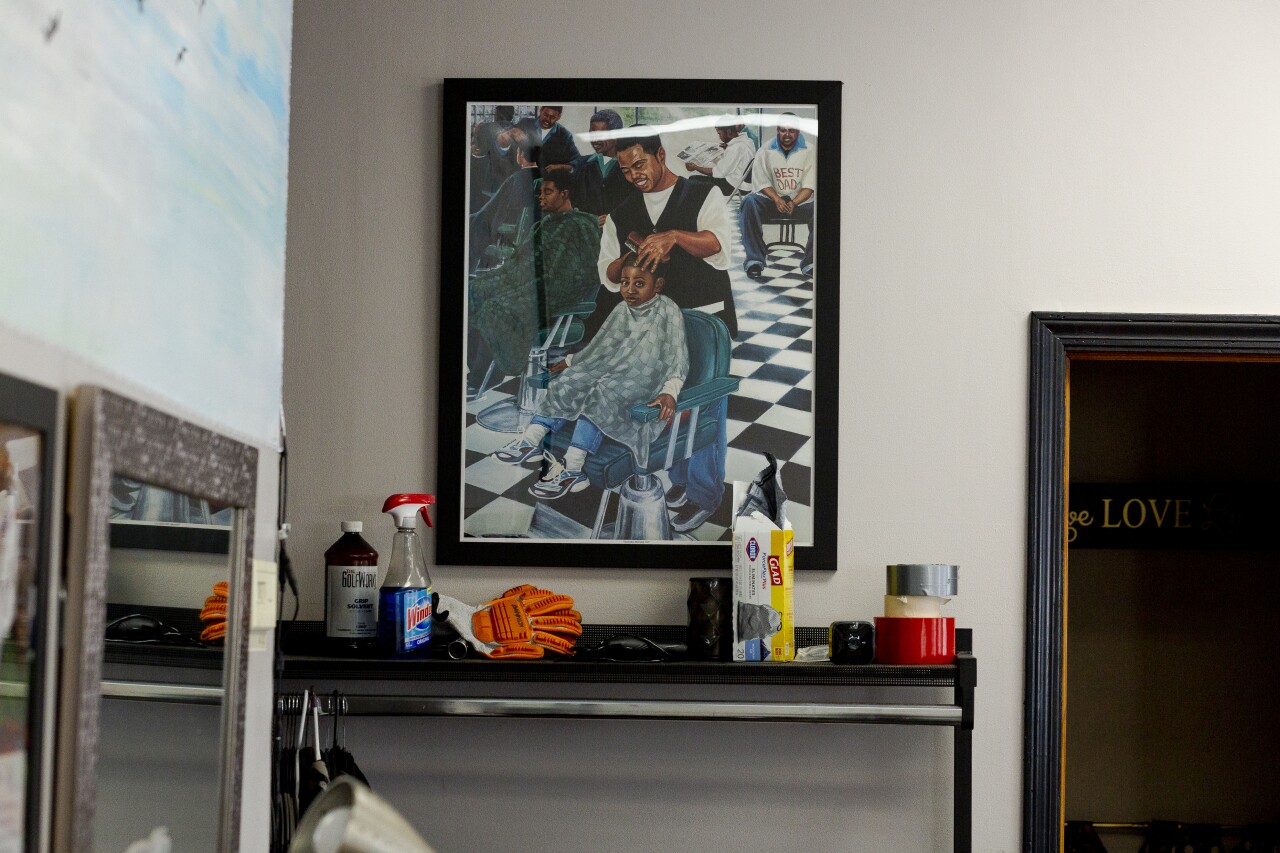 A poster of a Black barber adjusting the head of a Black child, wearing a cape while he sits on a chair.