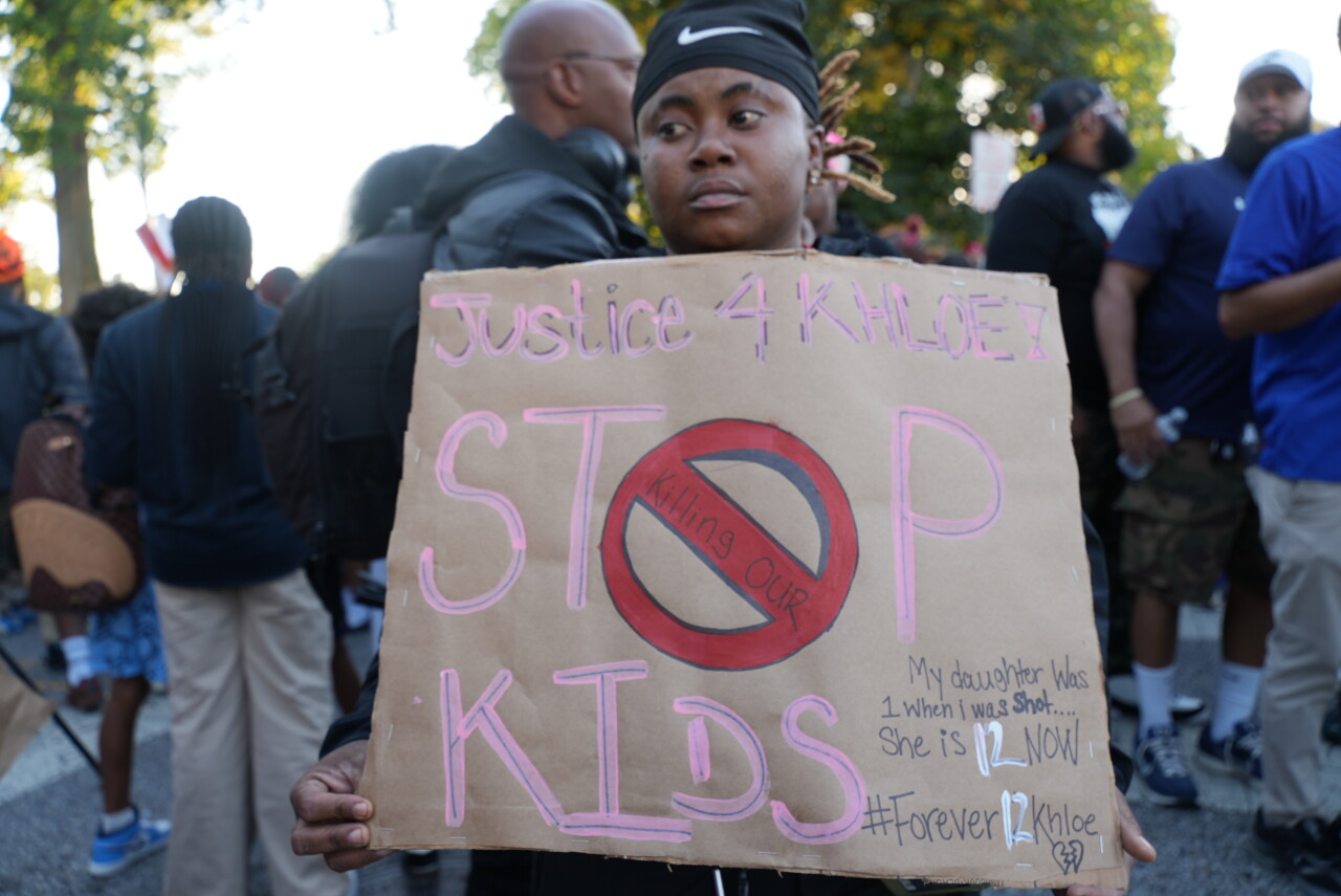 Community member with sign that reads "Stop killing our kids"