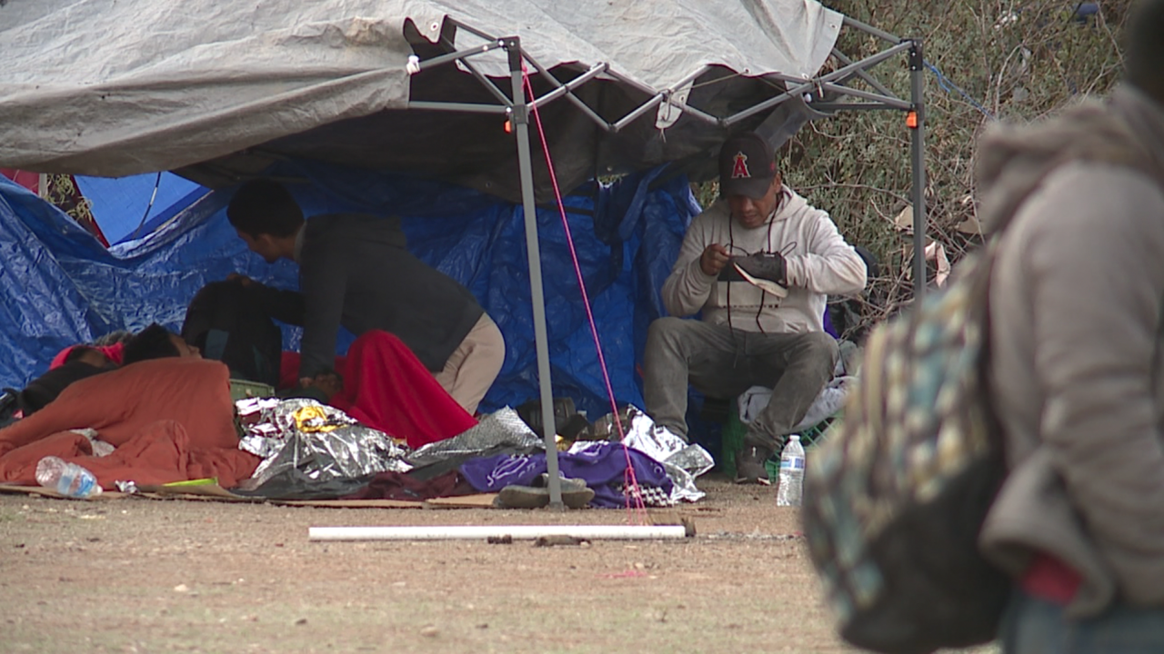 Migrants sit under a tarp, waiting for Border Patrol to arrive to detain and process them.