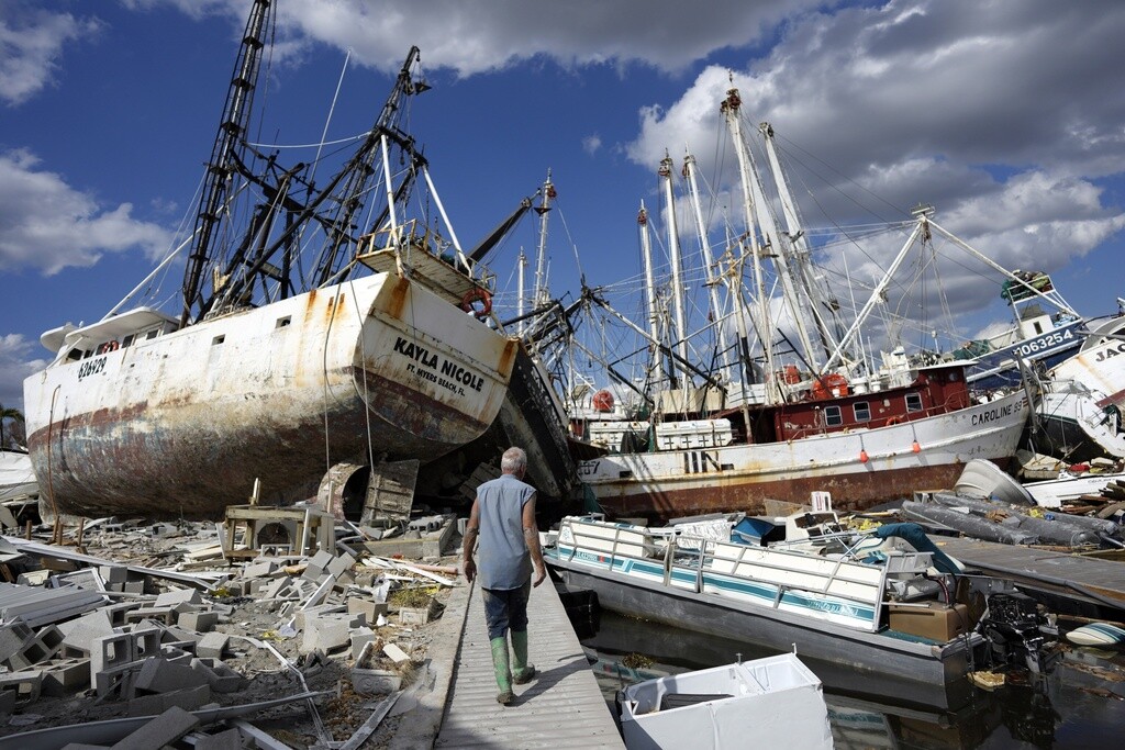 A man walks along a Florida waterfront littered with boats and debris after the passage of Hurricane Ian in 2022.