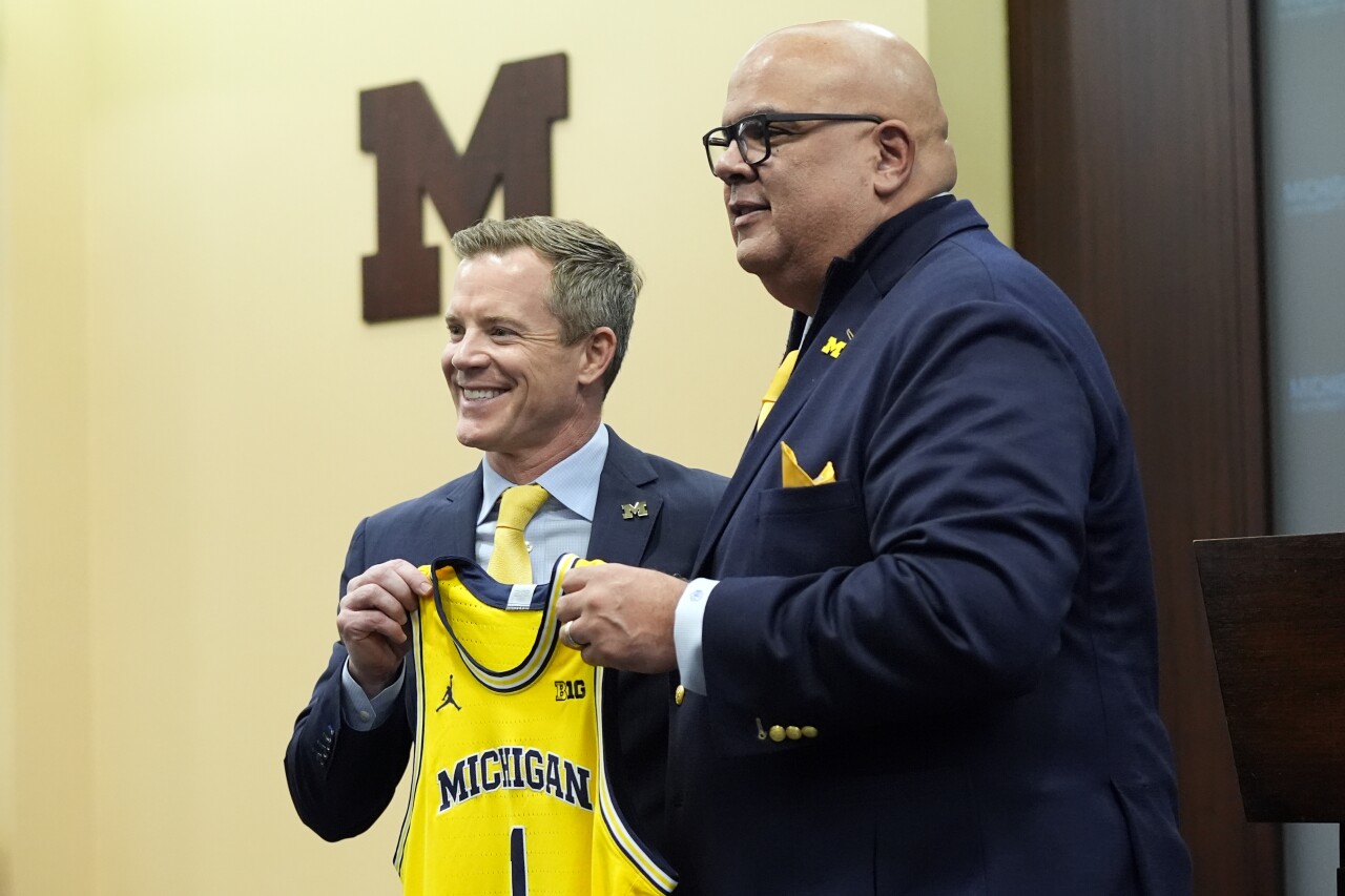 Michigan Wolverines basketball coach Dusty May and athletic director Warde Manuel hold basketball jersey during introductory news conference, March 26, 2024