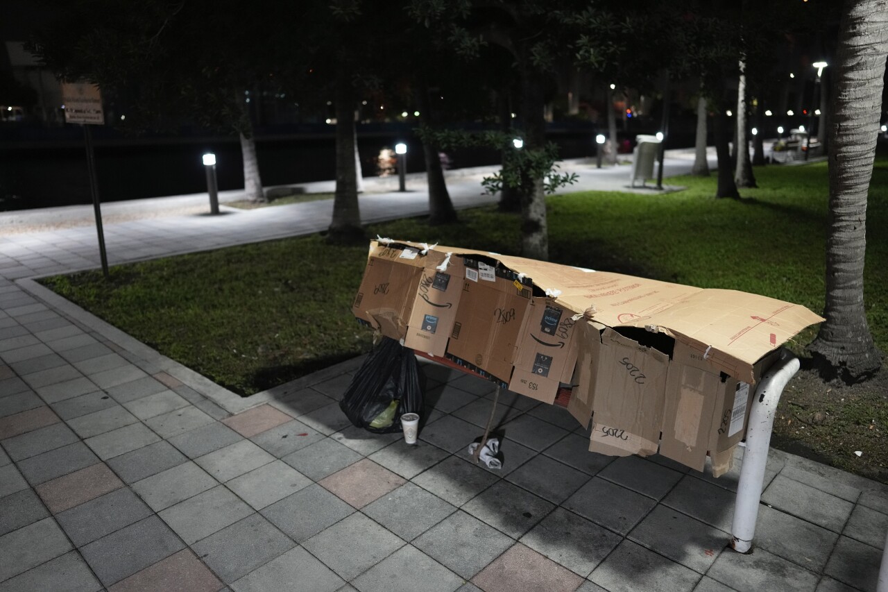 person sleeps in makeshift shelter on park bench in downtown Miami, Jan. 25, 2024
