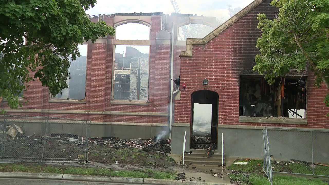 A photo of the building taken by a FOX 13 photojournalist. It's daytime, and smoke continues to billow out from within the now hollowed out building. The windows are blown out, and singed debris can be seen within and around the building.